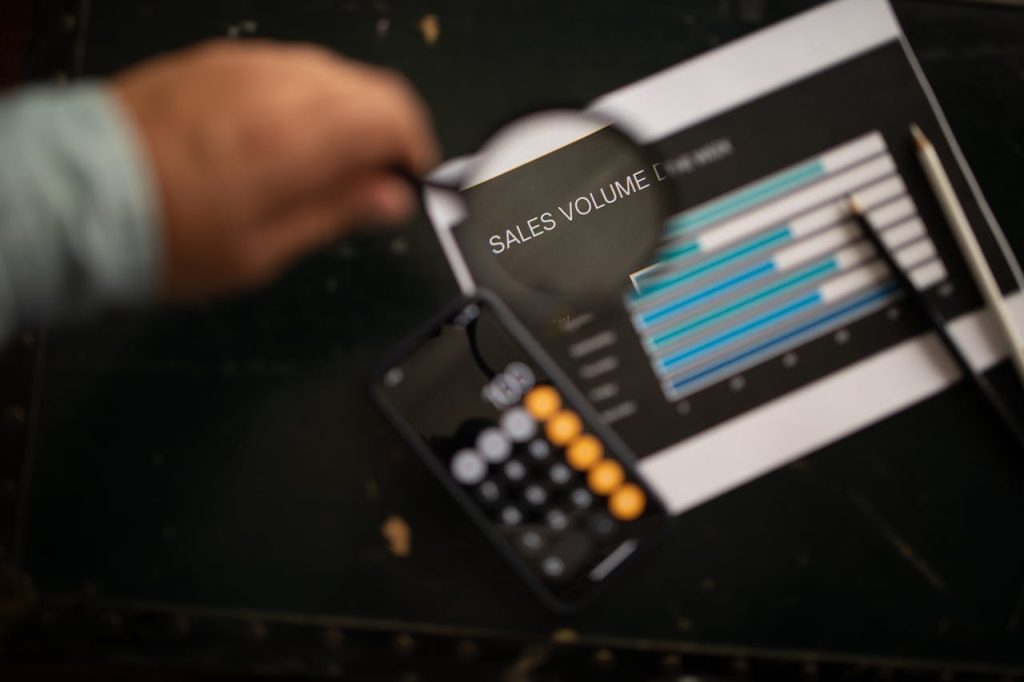 A focused examination of sales volume data using a magnifying glass and calculator.
